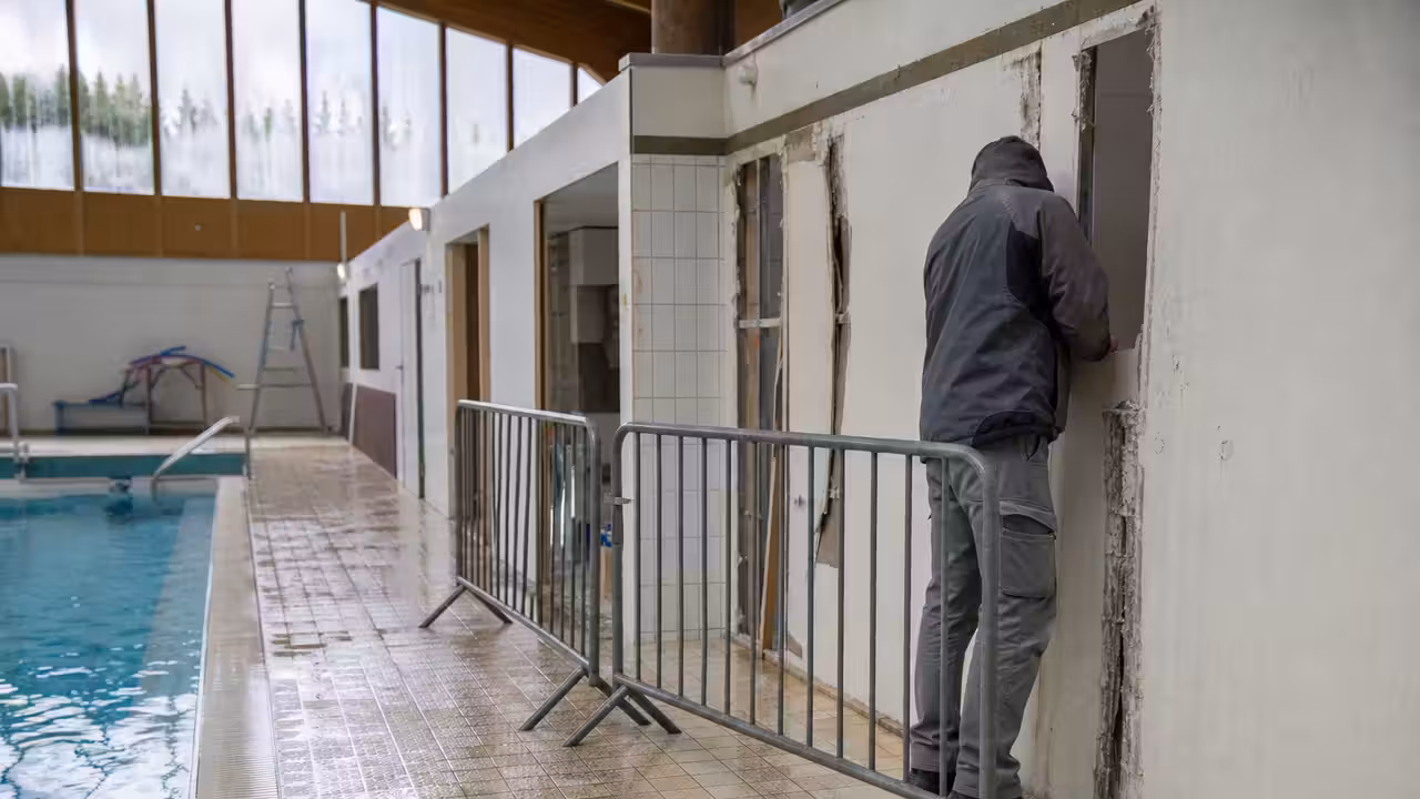 Bassin couvert municipal vide, avec barrières de sécurité près d’une cloison inspectée par un technicien