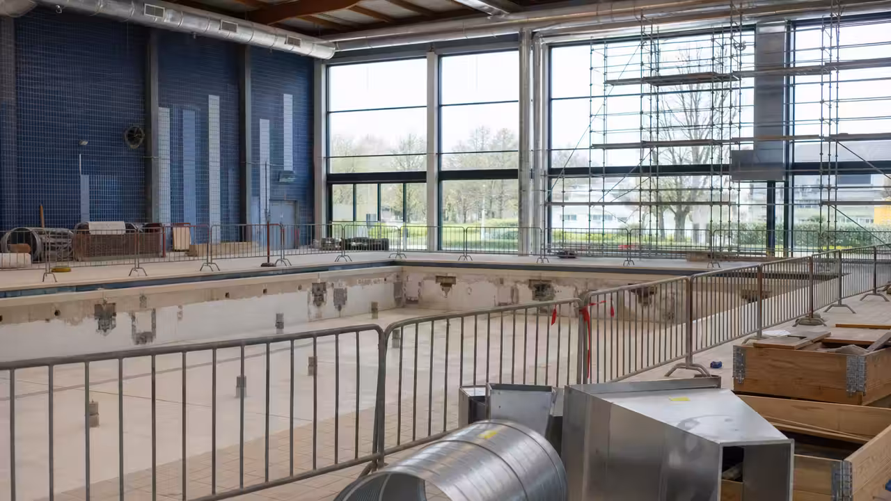 Intérieur d’une piscine municipale rénovée, avec bassin vide et équipes techniques en préparation