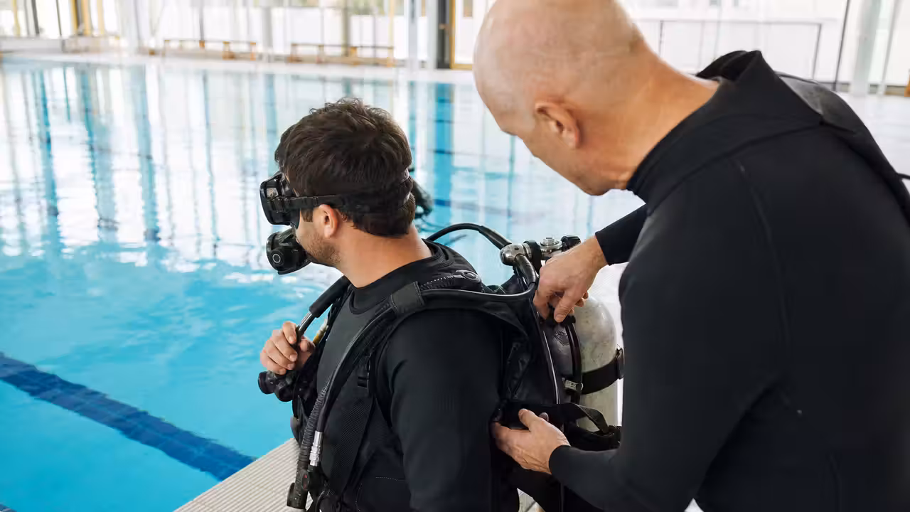 Un moniteur équipe un adulte d’un détendeur avant une première immersion dans une piscine couverte
