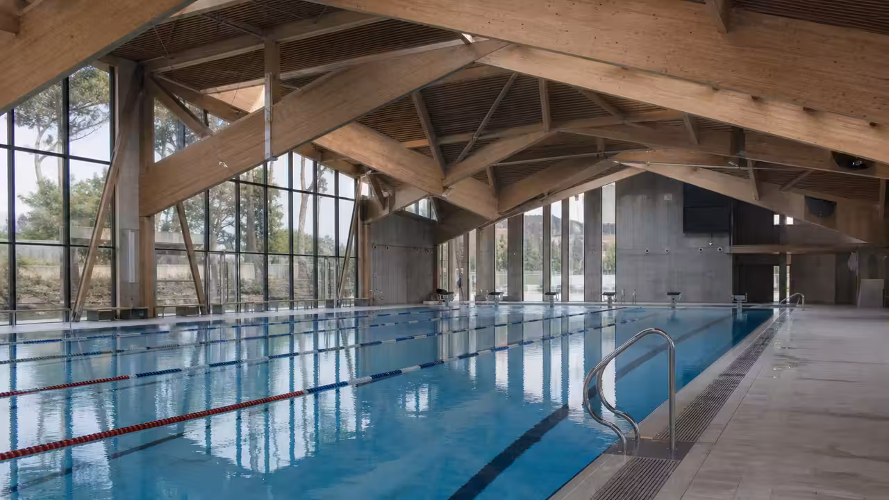 Intérieur lumineux d’une piscine publique contemporaine avec lignes d’eau, charpente et grandes baies vitrées