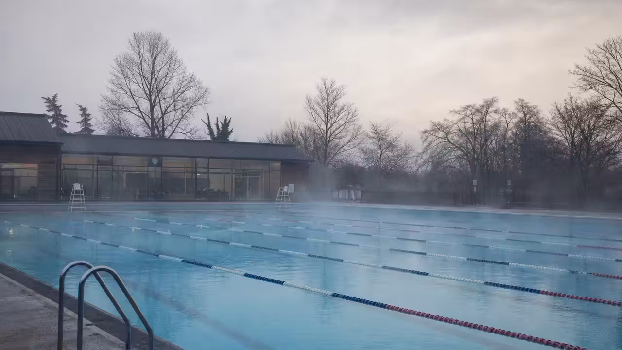 Bassin extérieur d’une piscine municipale vide en hiver, avec vapeur légère au-dessus de l’eau