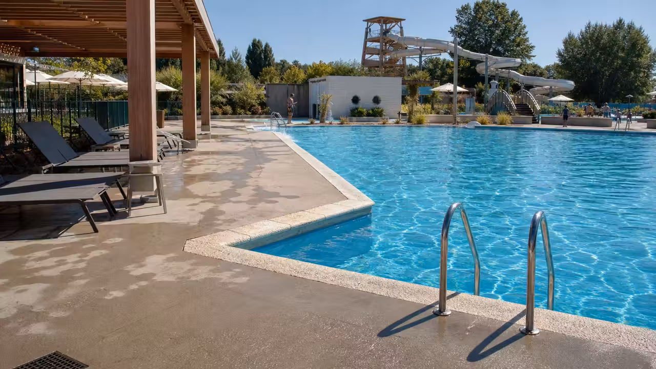 Bassin extérieur rénové avec pergola ombragée, transats et toboggan dans une base aqualudique estivale