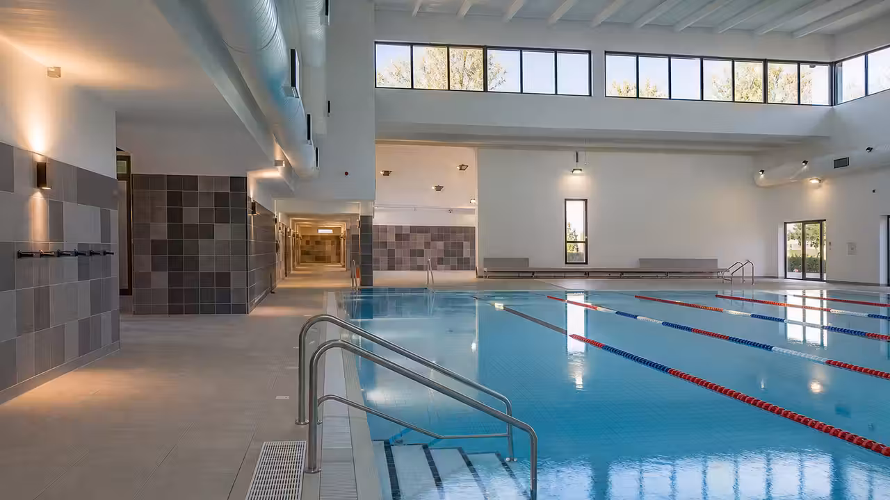 Bassin intérieur rénové avec lignes de nage, vestiaires lumineux et équipements techniques modernes en arrière-plan