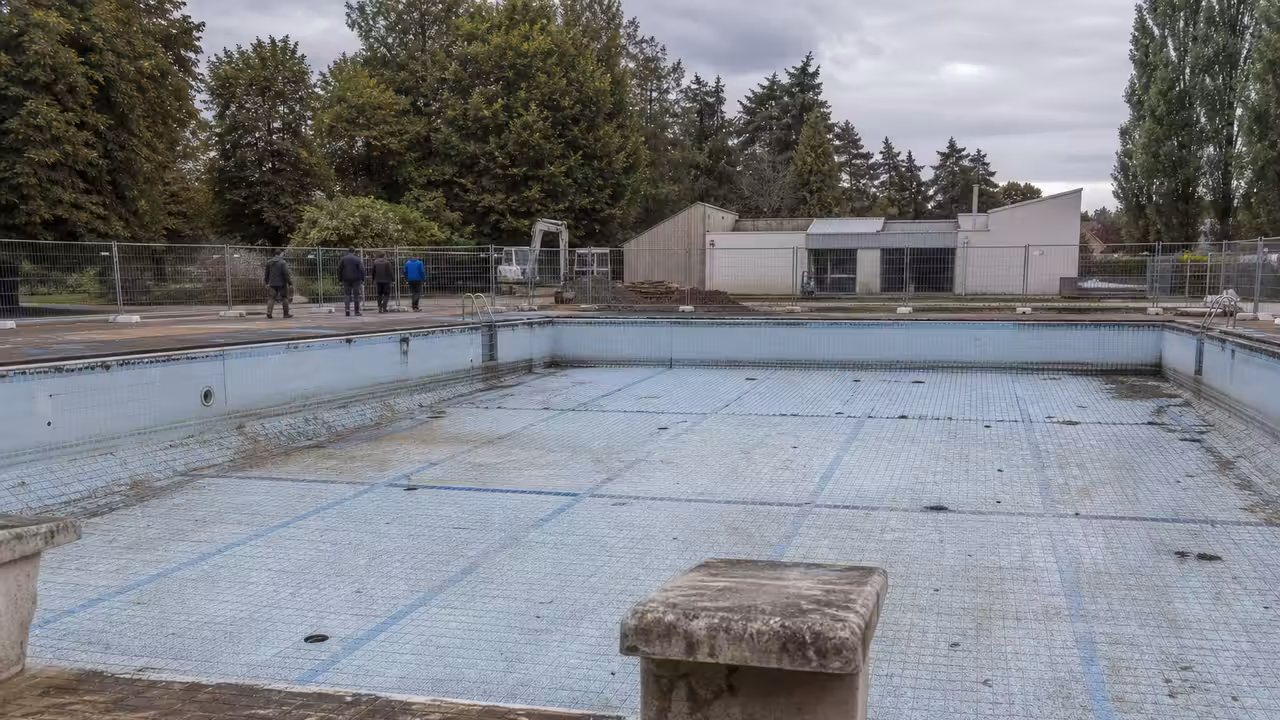 Site d’une ancienne piscine municipale clôturé, avec engins de chantier et matériaux triés en arrière-plan