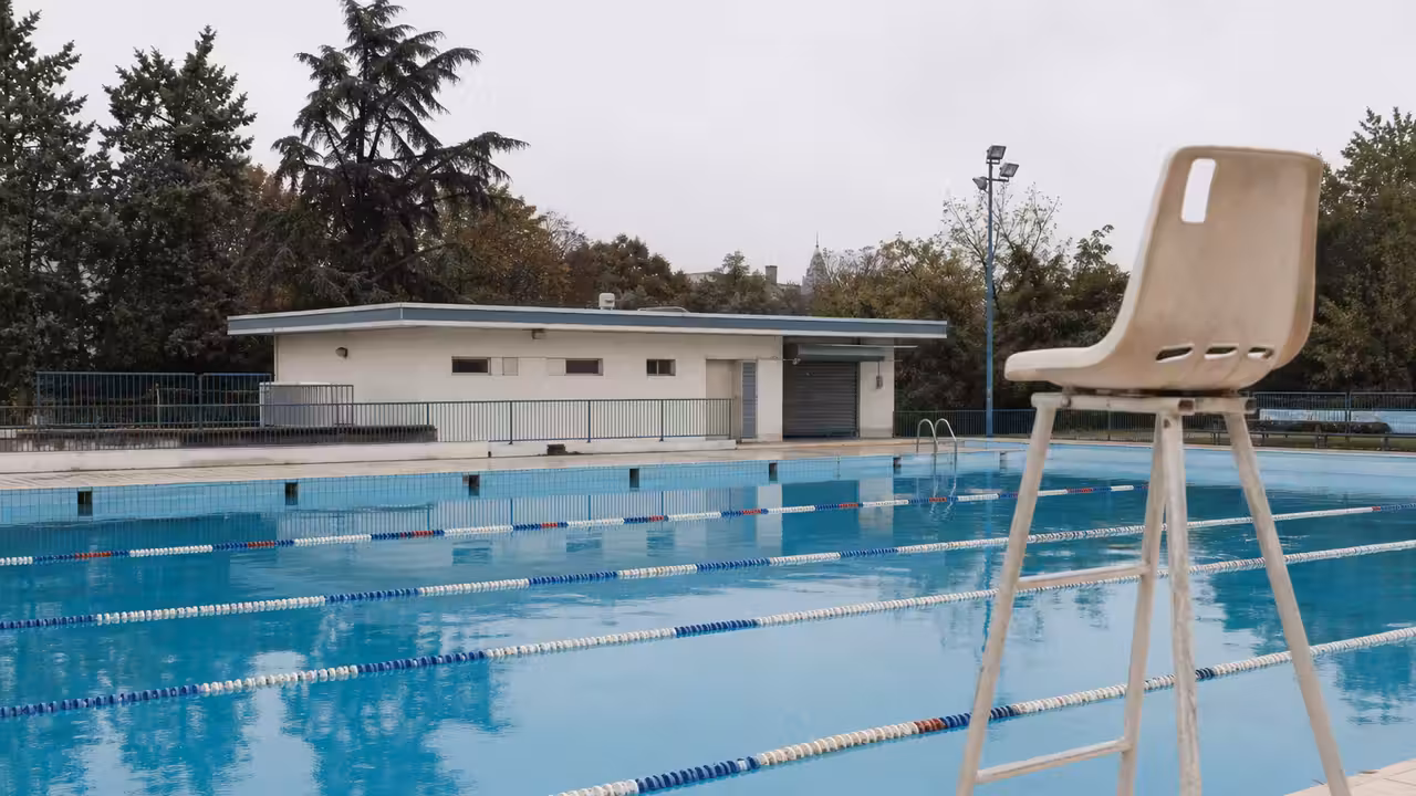 Bassin extérieur municipal vide avec lignes d’eau, vestiaires et arbres en arrière-plan à la lumière du matin