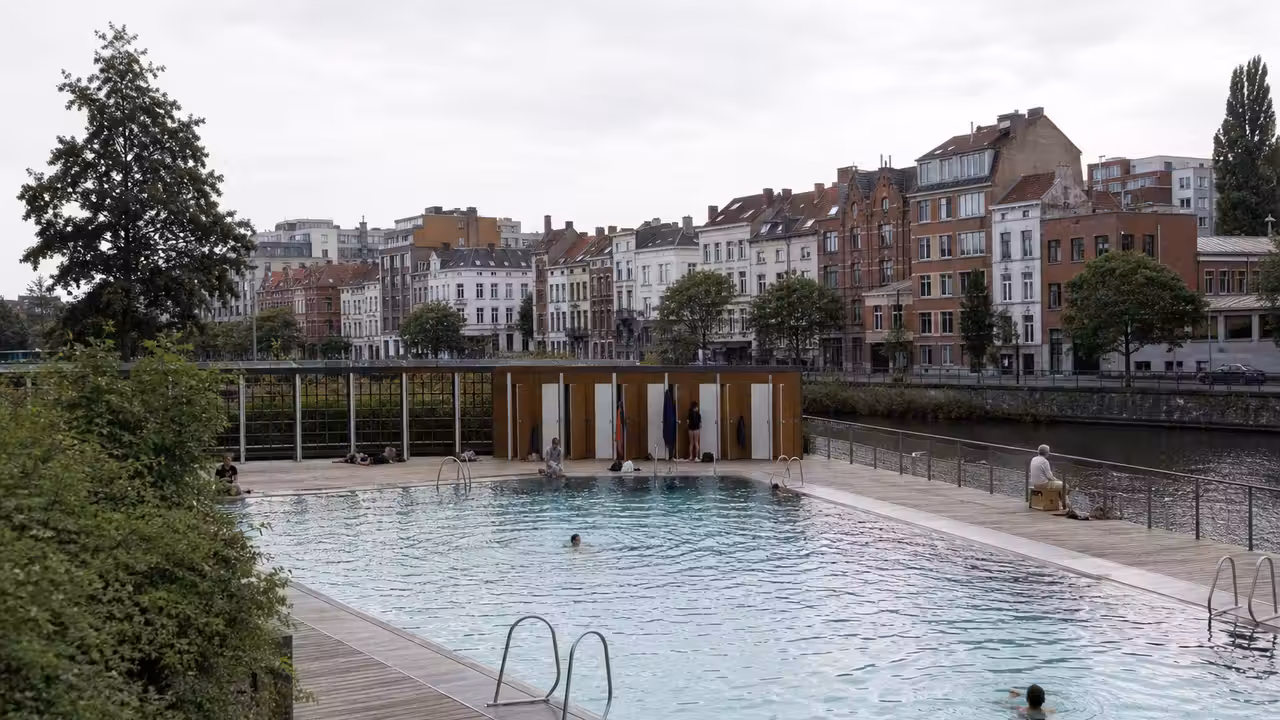 Bassin extérieur urbain au bord d'un canal, avec plages en bois et nageurs non identifiables
