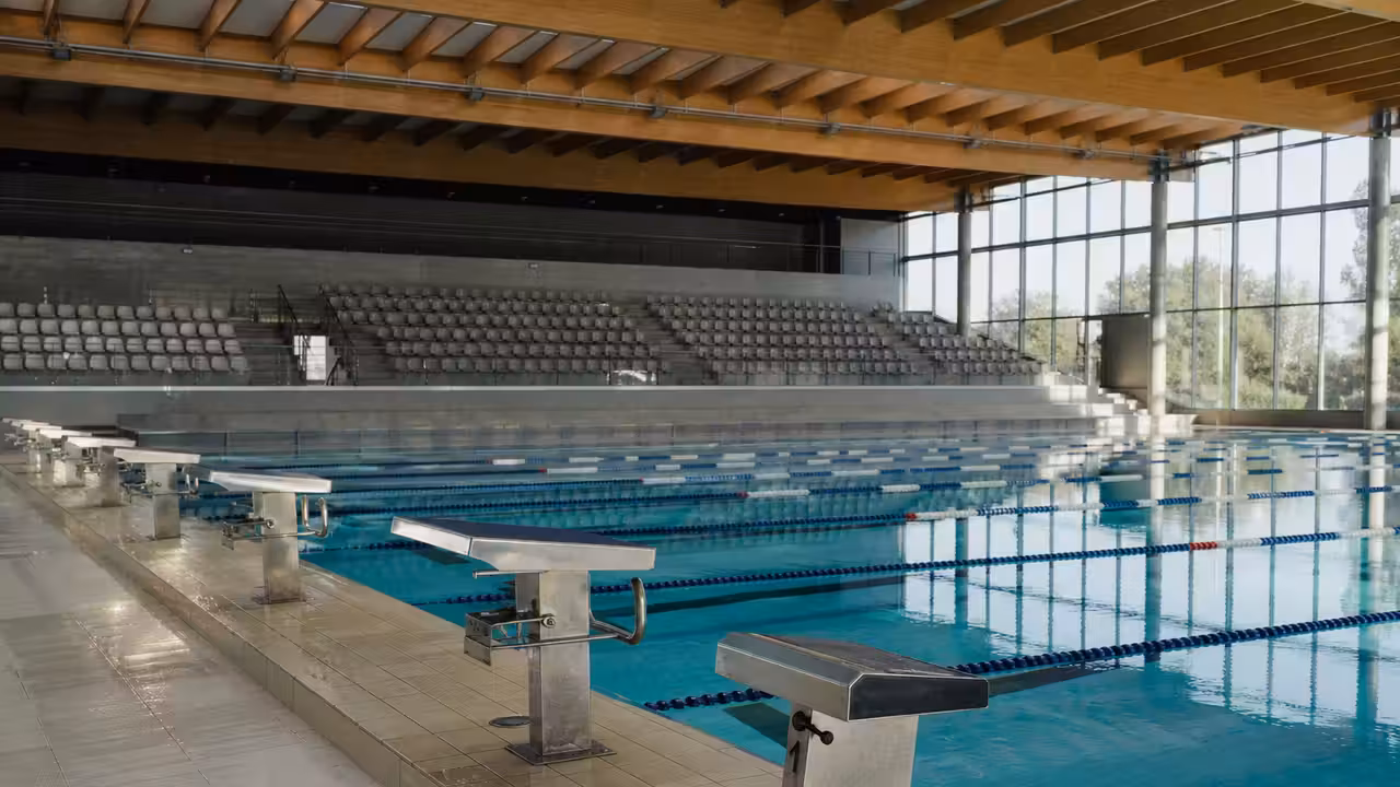 Vue intérieure d’un bassin sportif de 50 mètres avec lignes d’eau et gradins, baigné de lumière naturelle