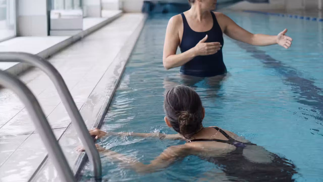 Adulte accompagné au bord d’un bassin municipal lors d’un exercice progressif de confiance dans l’eau