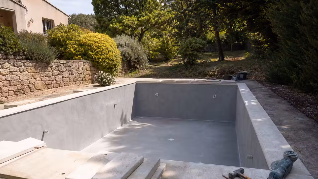 Piscine maçonnée en rénovation avec parois préparées, margelles déposées et outils de chantier au premier plan