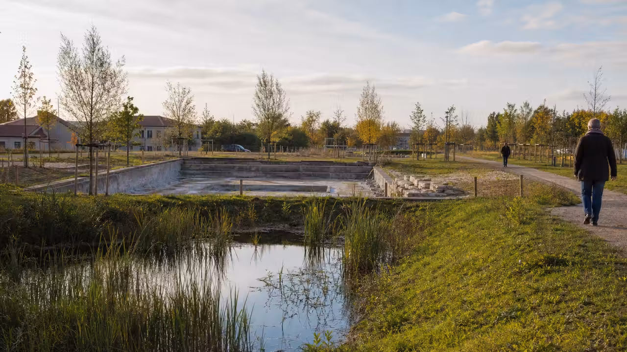 Ancien bassin municipal en cours de reconversion paysagère avec végétation, cheminements et espace public