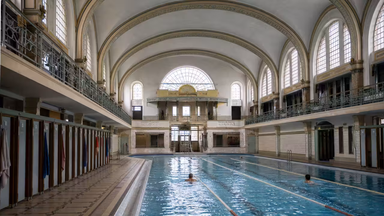 Halle de bassin historique rénovée avec voûte restaurée, lignes d’eau et lumière naturelle à Paris