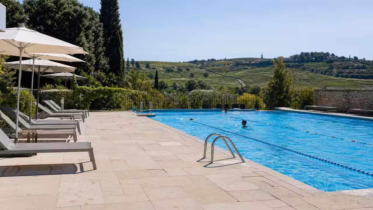 Bassin extérieur d’une piscine associative avec lignes d’eau, transats et végétation provençale en été