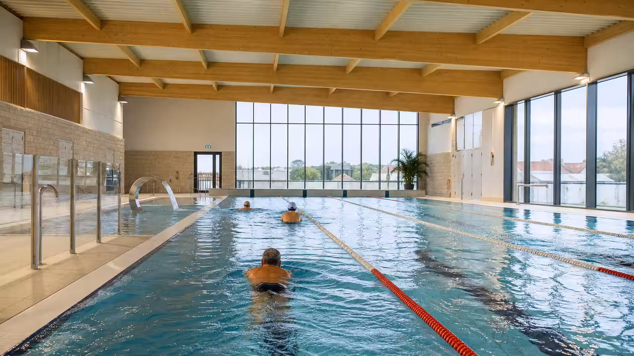 Bassin sportif couvert de 25 mètres dans une piscine publique rénovée, avec lignes d’eau et baies vitrées