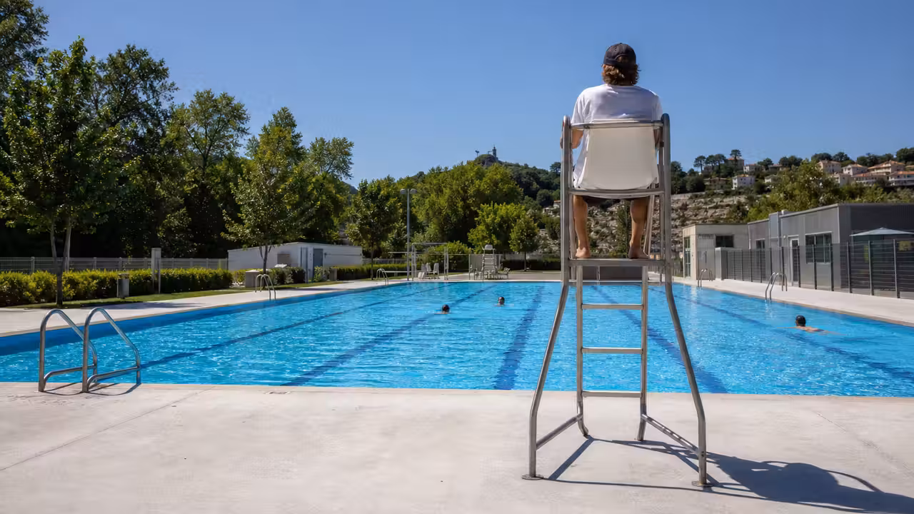 Bassin extérieur d’une piscine publique avec nageurs éloignés et maître-nageur surveillant depuis le bord