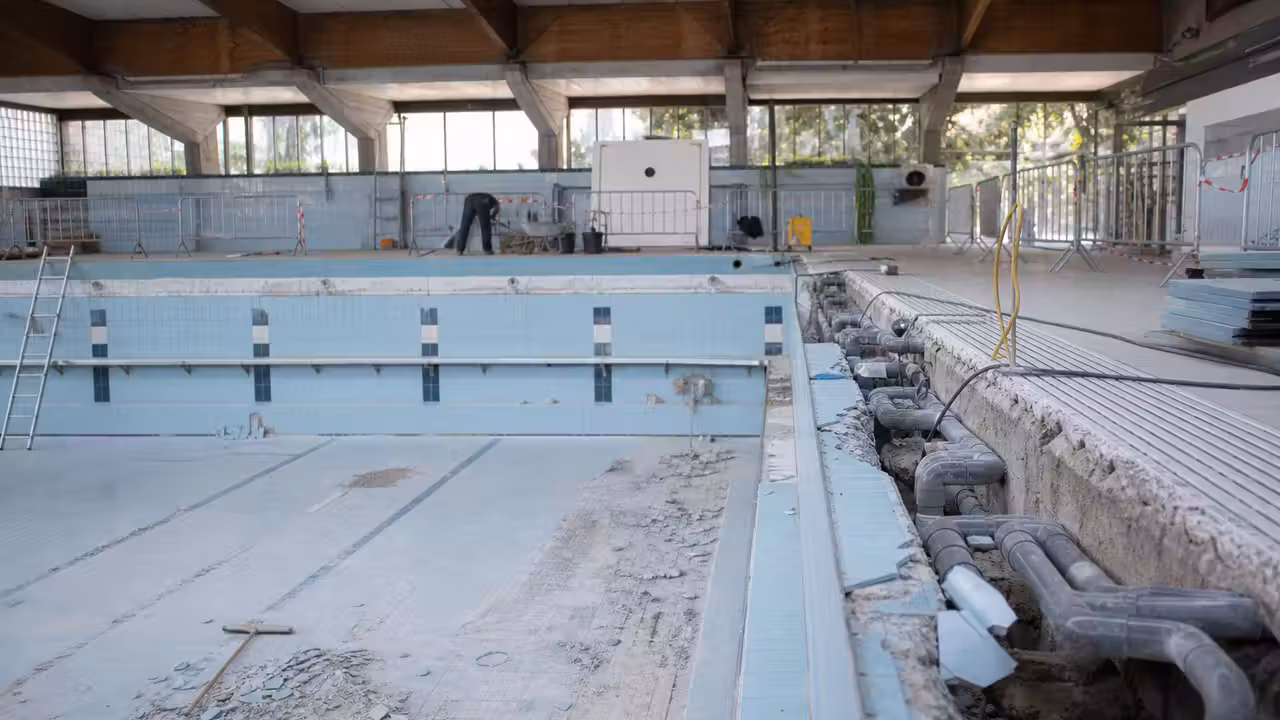 Bassin municipal vide en rénovation, avec carrelage déposé et équipements techniques en intervention