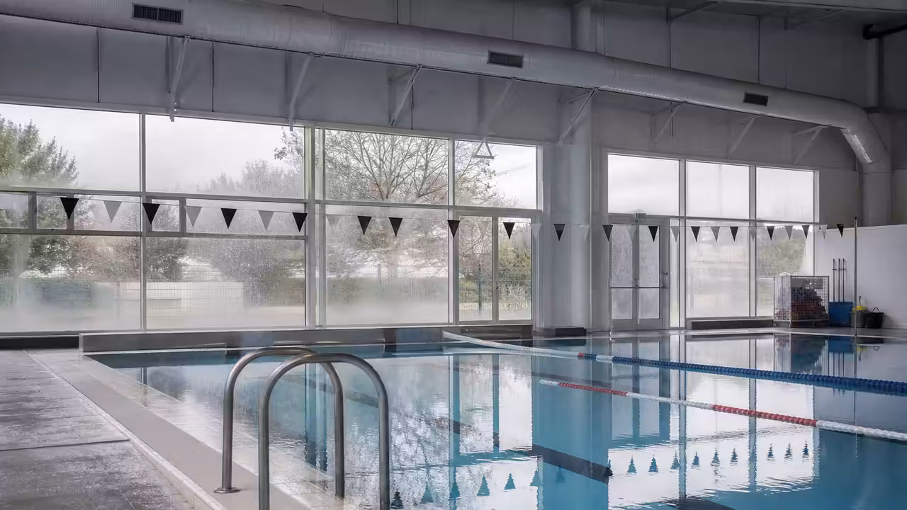 Bassin couvert vide, lignes d’eau et réseau de ventilation métallique dans un centre aquatique municipal