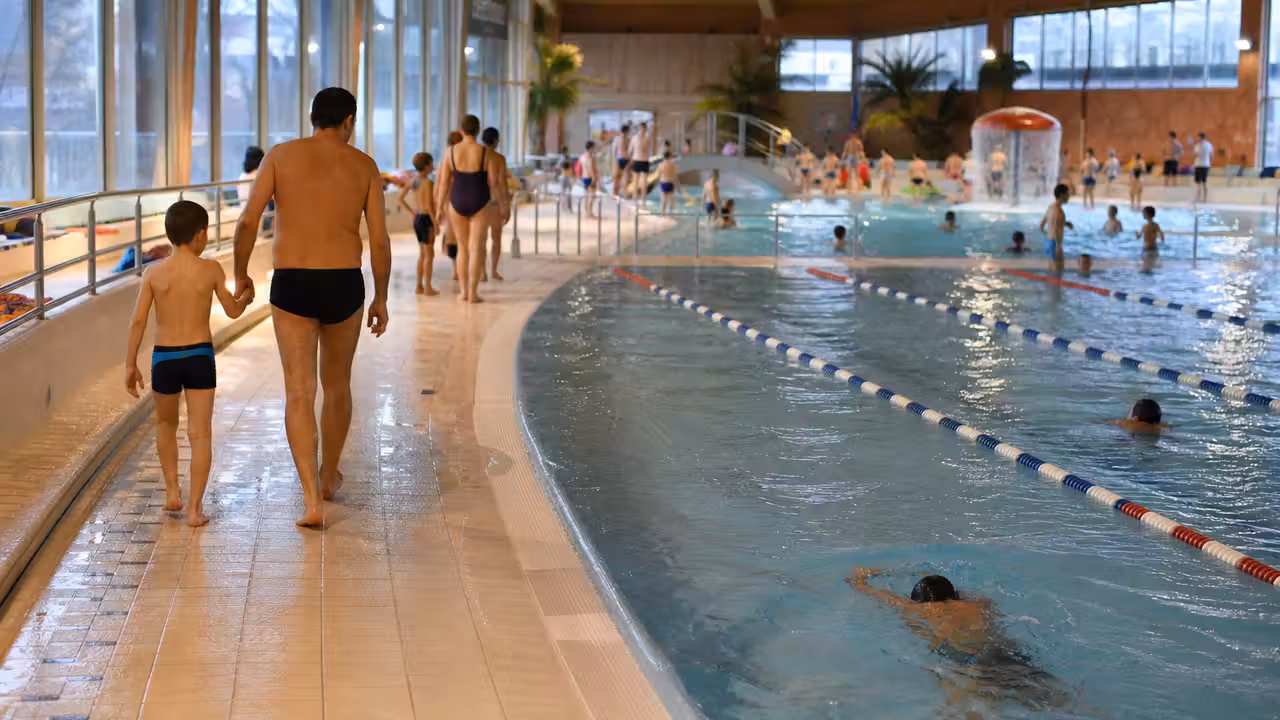 Bassin couvert lumineux avec lignes de nage, espace ludique et familles pendant les vacances d’hiver