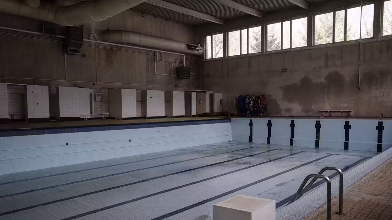 Bassin municipal vide avec lignes d’eau, carrelage humide et hall aquatique éclairé par la lumière du jour