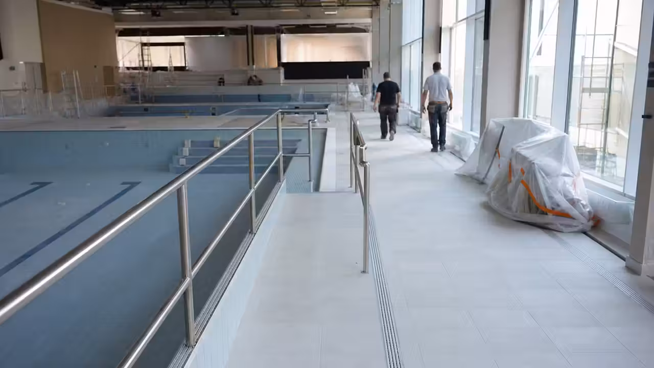 Entrée fermée d’une piscine publique avec barrières de chantier devant un bâtiment aquatique en rénovation