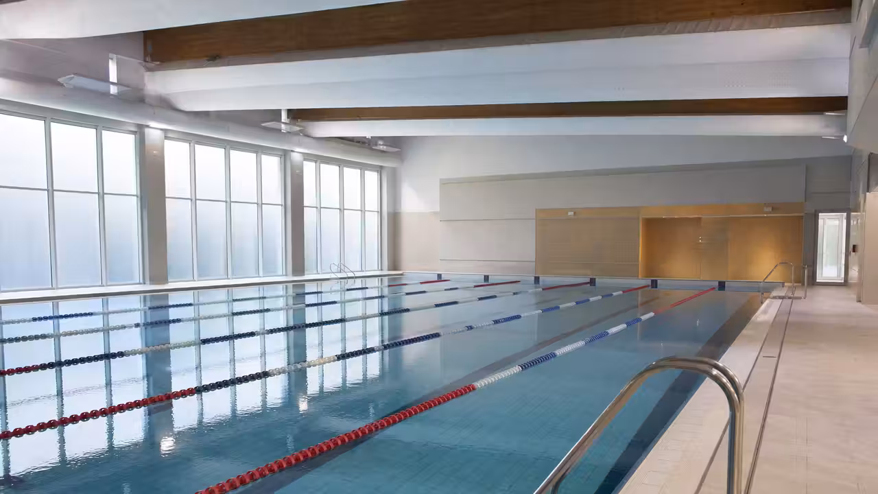 Bassin sportif rénové de 25 mètres dans une piscine publique, avec lignes d’eau et baies vitrées