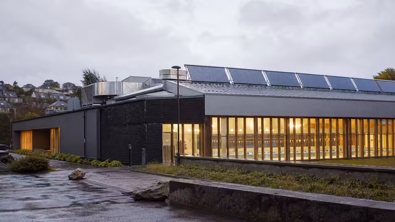 Toiture équipée de capteurs solaires au-dessus d’un bassin public, avec vitrages et espace technique visibles