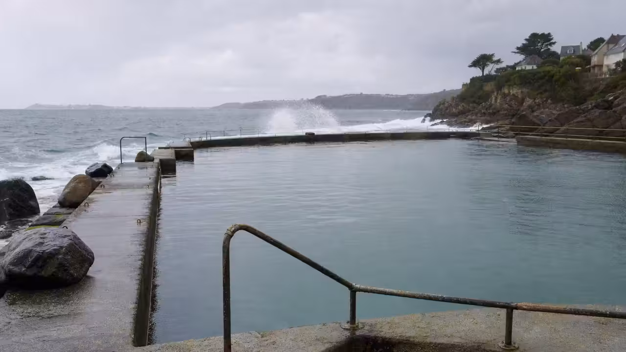 Bassin d’eau de mer en bord de côte, entouré d’un ouvrage minéral exposé aux vagues et aux embruns.