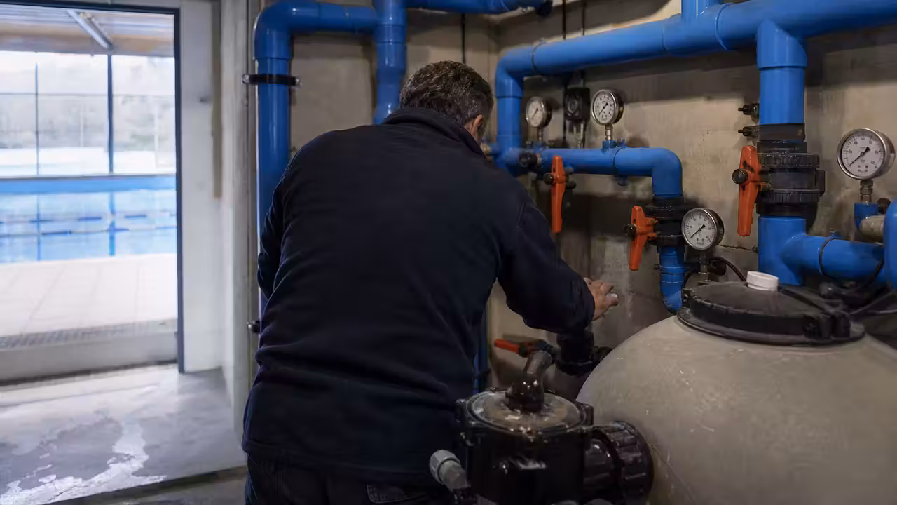 Technicien contrôlant les vannes et canalisations d’un local technique de piscine publique après une fuite