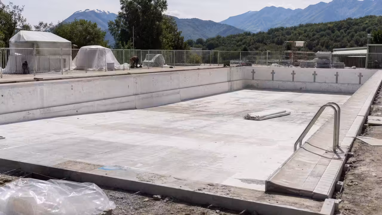 Bassin municipal vide en rénovation, avec barrières de chantier et équipements techniques à l’arrière-plan