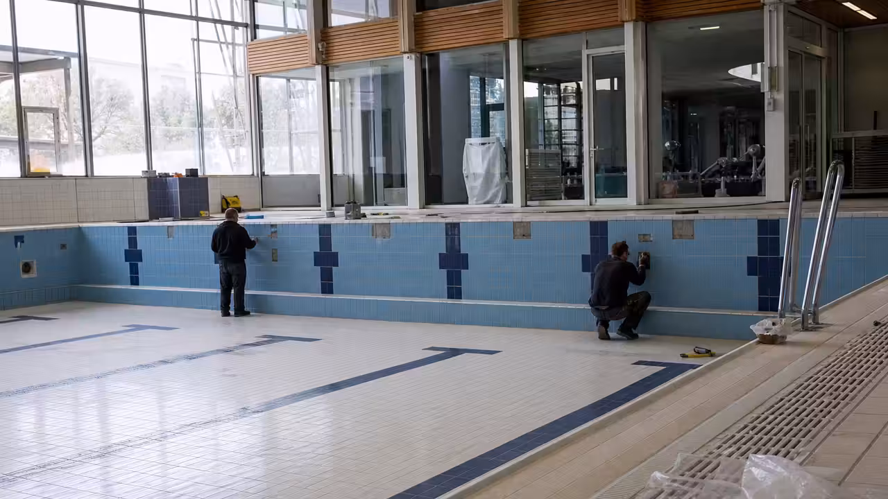 Bassin municipal vide en rénovation, avec contrôle des joints et équipements techniques en arrière-plan