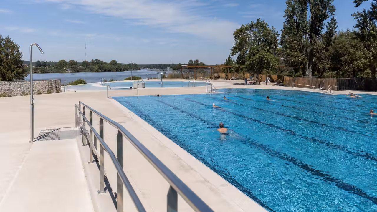 Bassin extérieur rénové d’une piscine publique avec plages minérales, lignes d’eau et végétation en bord de Loire
