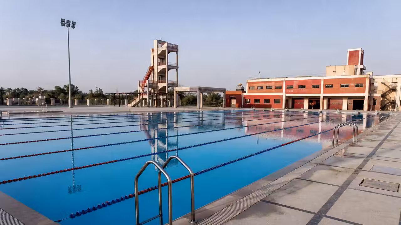 Bassin de 25 mètres vide, lignes d’eau et plage antidérapante dans un centre aquatique municipal.