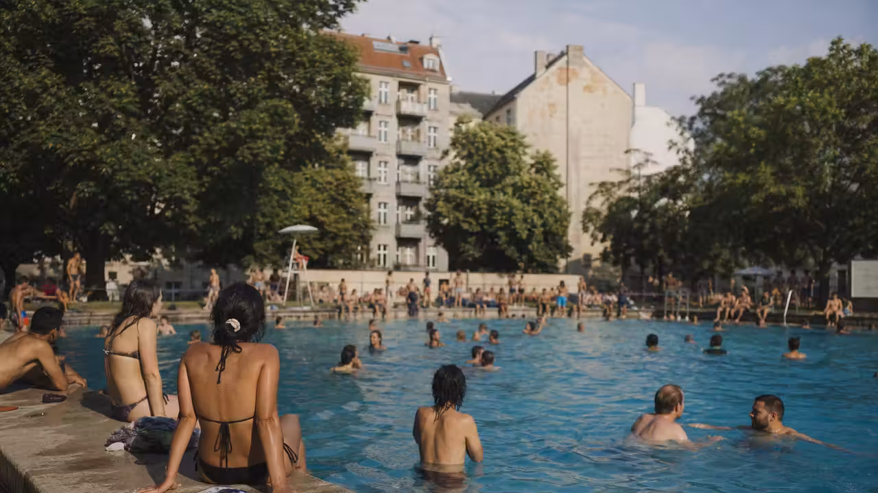 Bassin extérieur fréquenté lors d’une journée d’été, avec plages, baigneurs et végétation urbaine