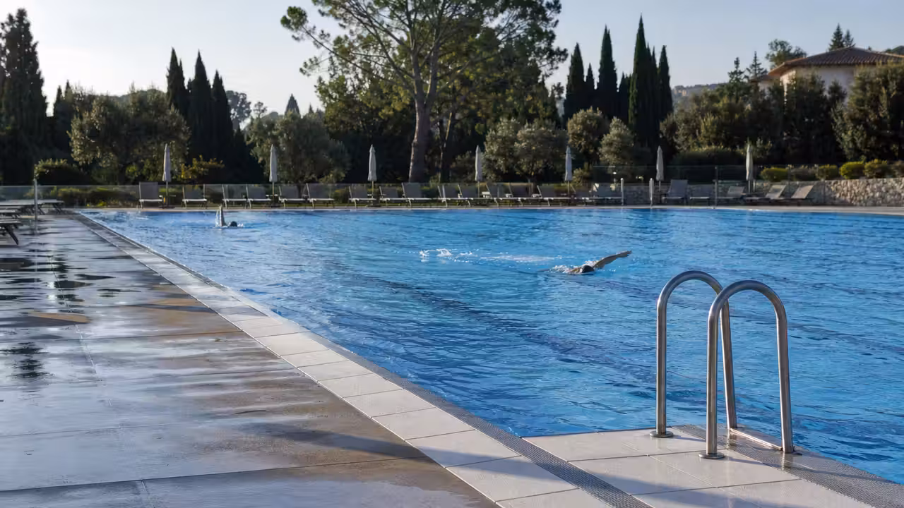 Nageur dans un bassin extérieur au printemps, avec lignes d’eau et végétation en arrière-plan