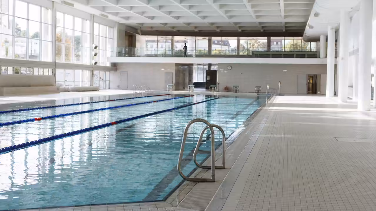 Bassin couvert rénové avec lignes de nage, baies vitrées et ventilation moderne dans une piscine municipale