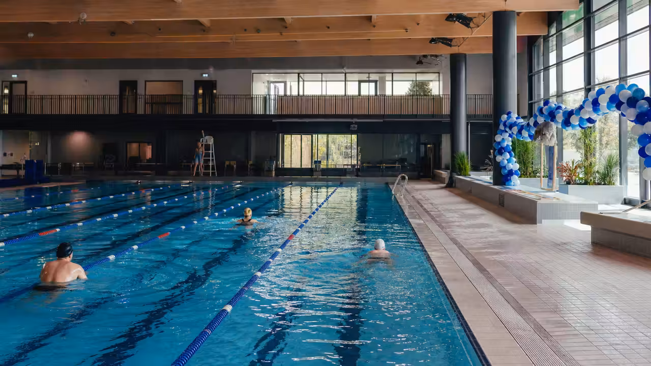 Bassin couvert lumineux d’un centre aquatique public avec lignes de nage et baigneurs au loin