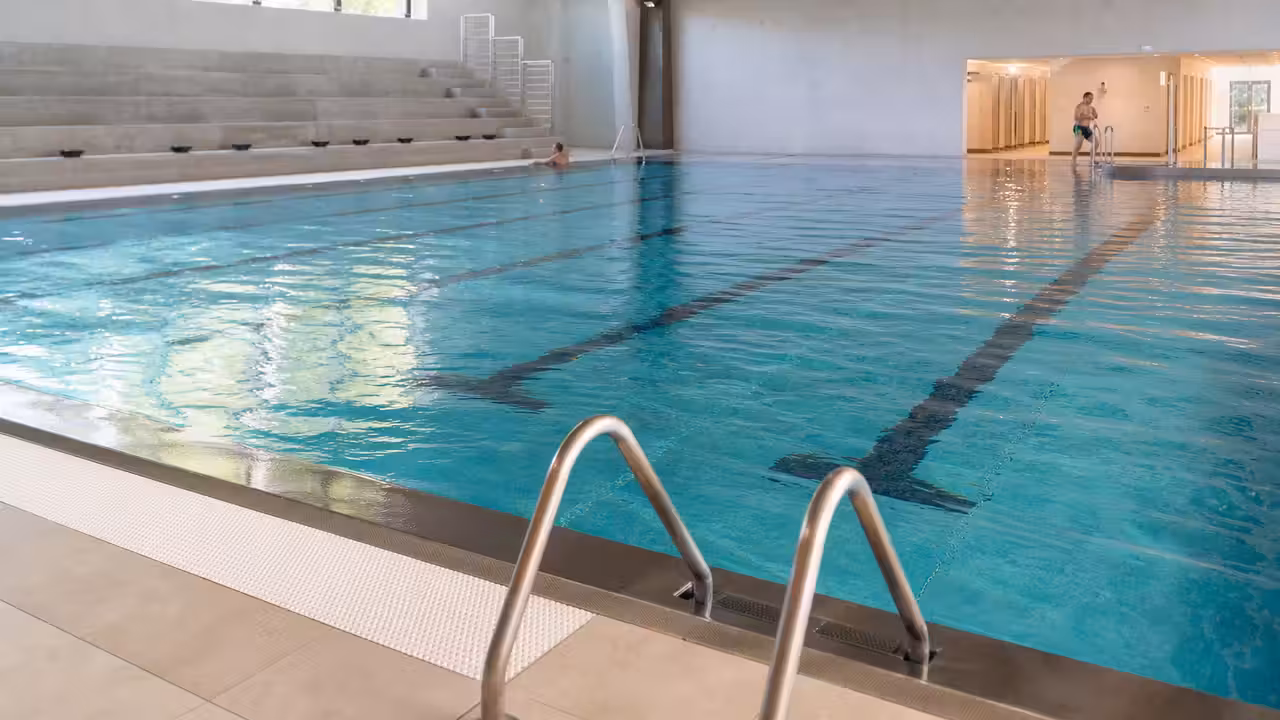 Bassin municipal rénové avec parois en inox, lignes d’eau et vestiaires lumineux en arrière-plan