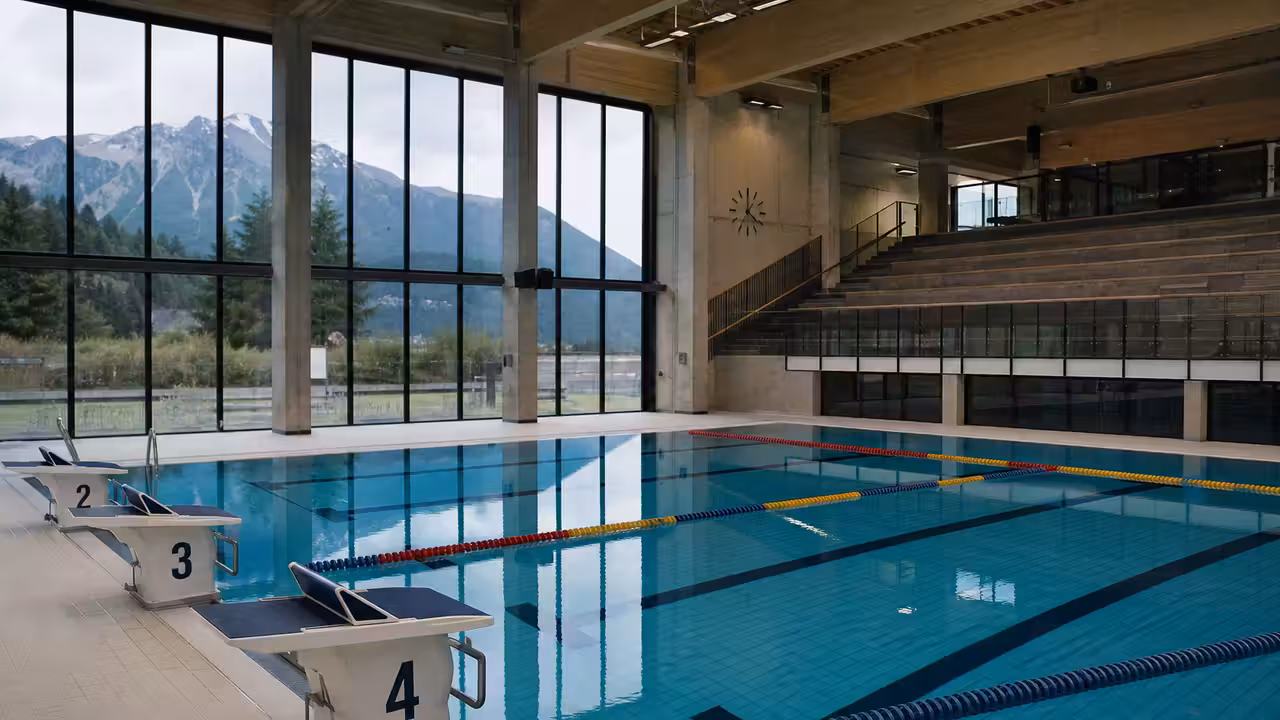 Bassin sportif couvert avec lignes d’eau, plots de départ et gradins vides prêts pour une compétition