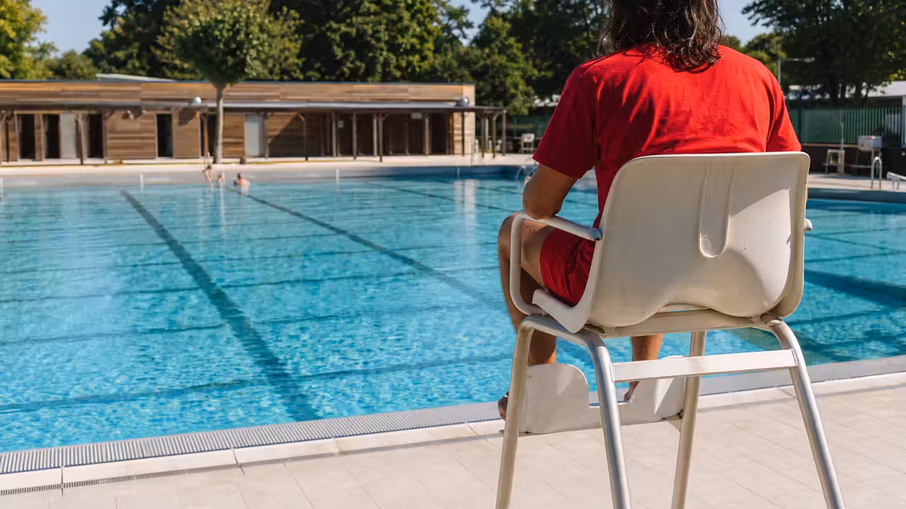 Bassin extérieur d’une piscine municipale avec lignes d’eau, plage minérale et arbres en été
