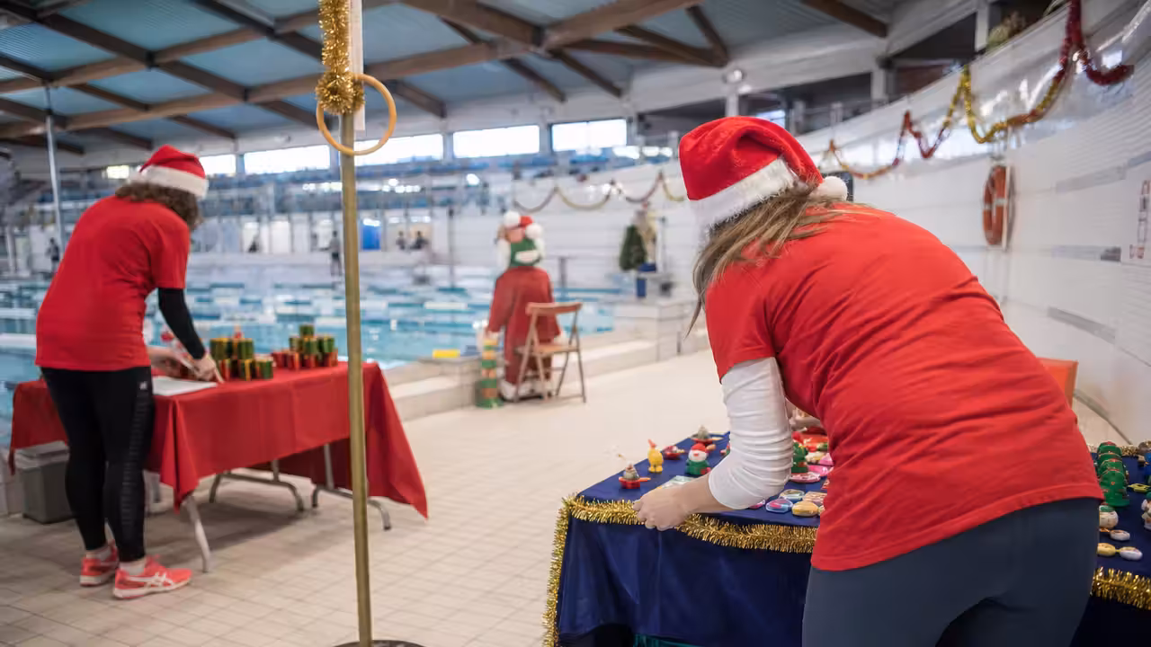 Bénévoles préparant des stands de jeux festifs au bord d’un bassin couvert décoré pour Noël