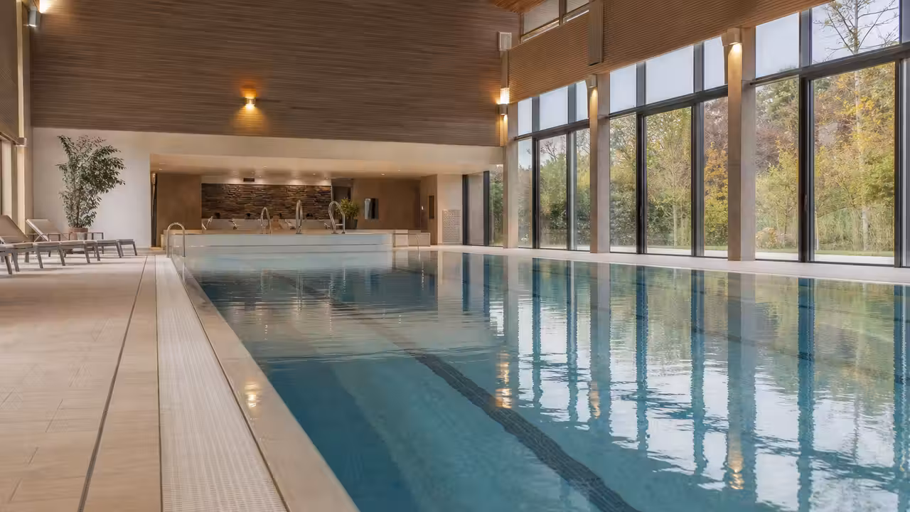Bassin intérieur lumineux d’un centre aquatique avec lignes d’eau, banquettes balnéo et eau calme chauffée