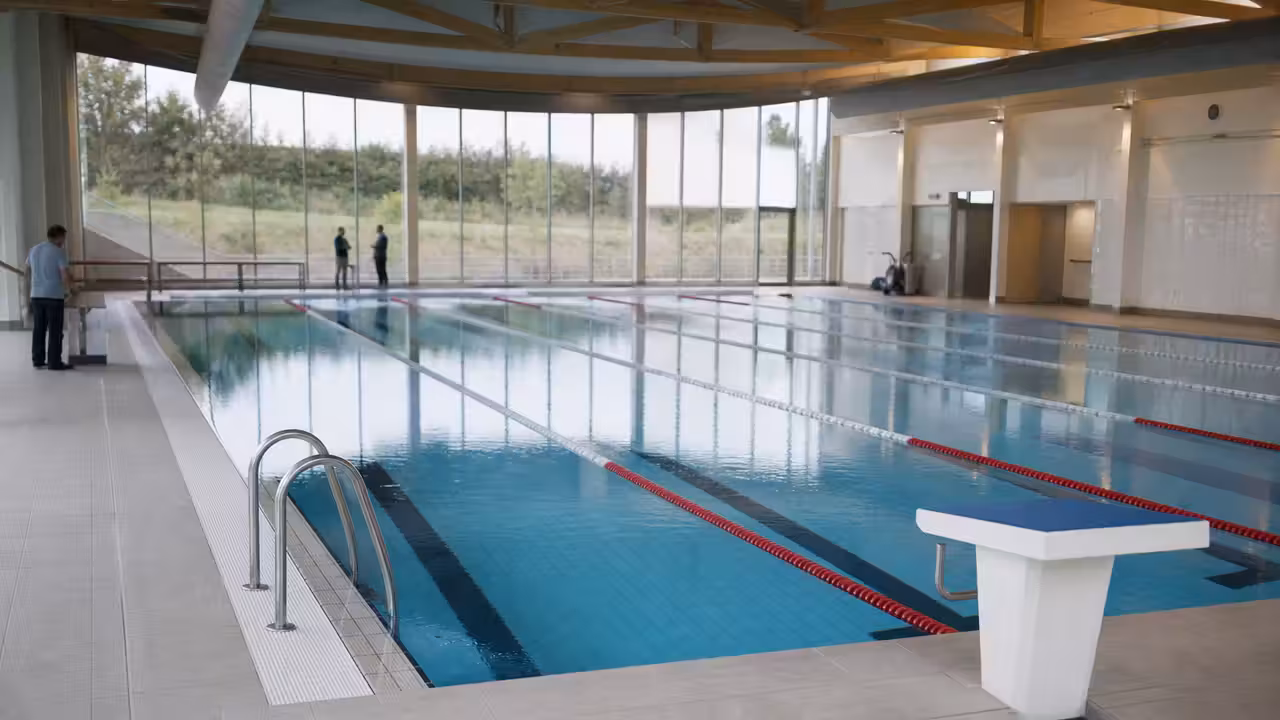Intérieur lumineux d’une piscine municipale rénovée avec bassin sportif, lignes d’eau et gradins vides