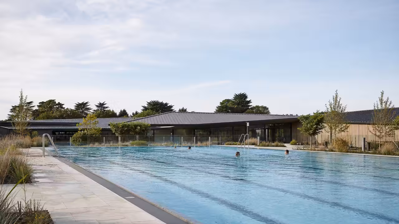 Bassin extérieur contemporain avec lignes de nage, plage claire et végétation bretonne sous une lumière d’été
