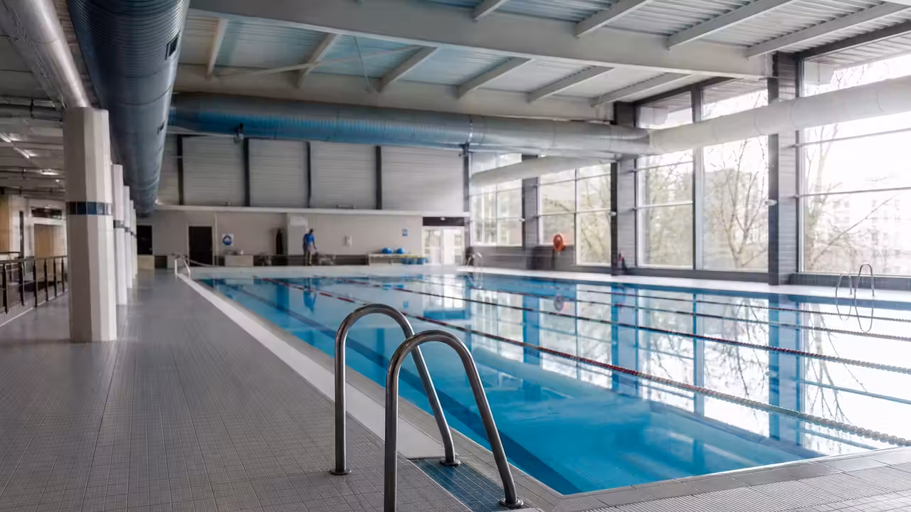Halle de piscine municipale vide avec lignes d’eau, baies vitrées et système de ventilation au plafond