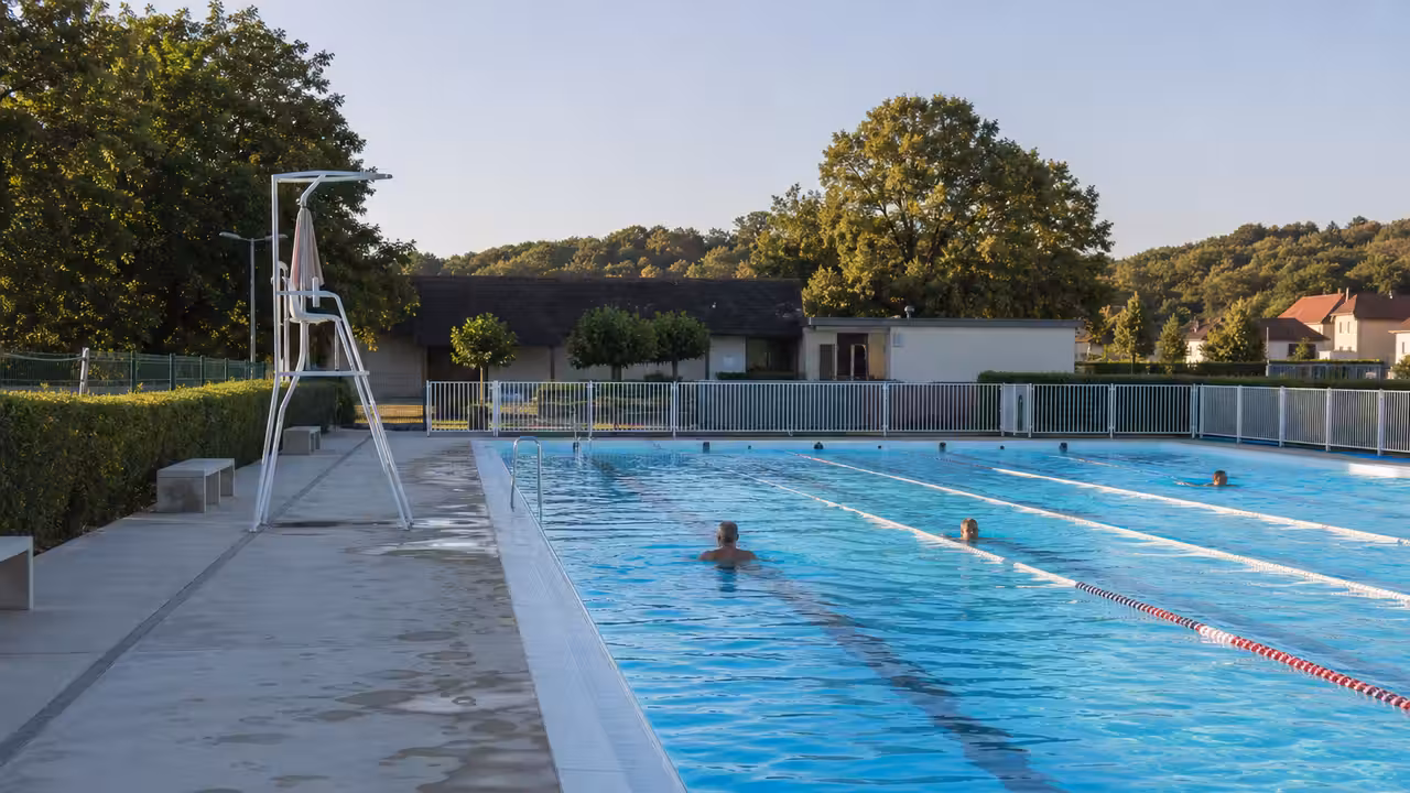 Bassin municipal extérieur calme avec lignes d’eau, plage minérale et cabine de surveillance sous le soleil