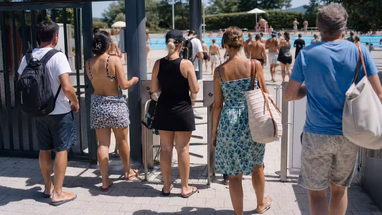 Entrée d’une piscine municipale en été, avec des baigneurs attendant devant le contrôle d’accès