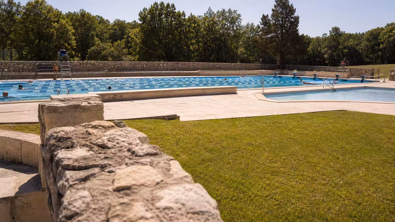 Bassins extérieurs d’une piscine municipale avec lignes de nage et pelouse, sous une lumière estivale