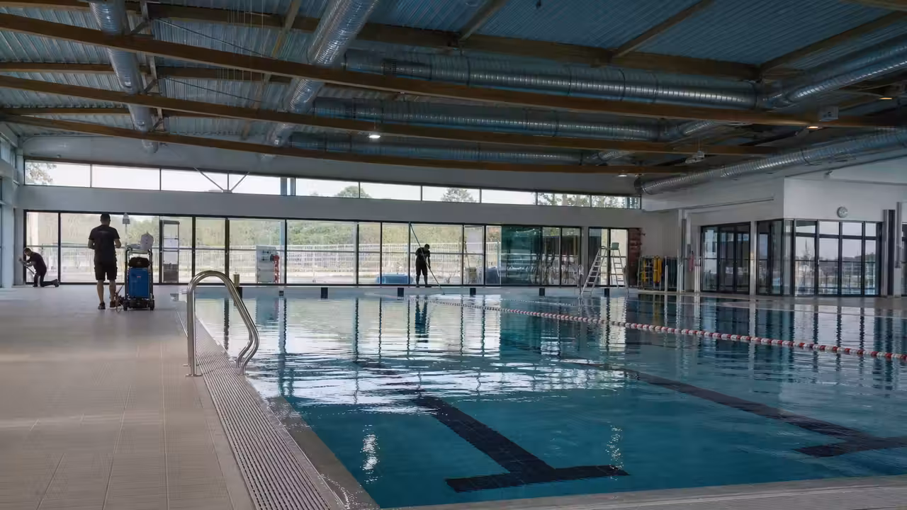 Hall de piscine couverte vide avec lignes d’eau, baies vitrées et réseau de ventilation au plafond