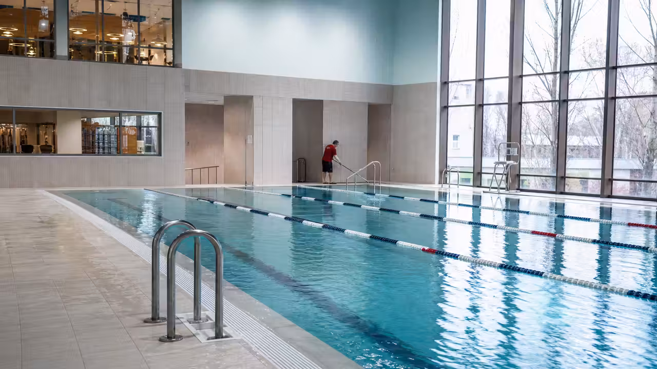 Bassin intérieur rénové d’une piscine publique avec lignes d’eau, vestiaires lumineux et personnel en préparation