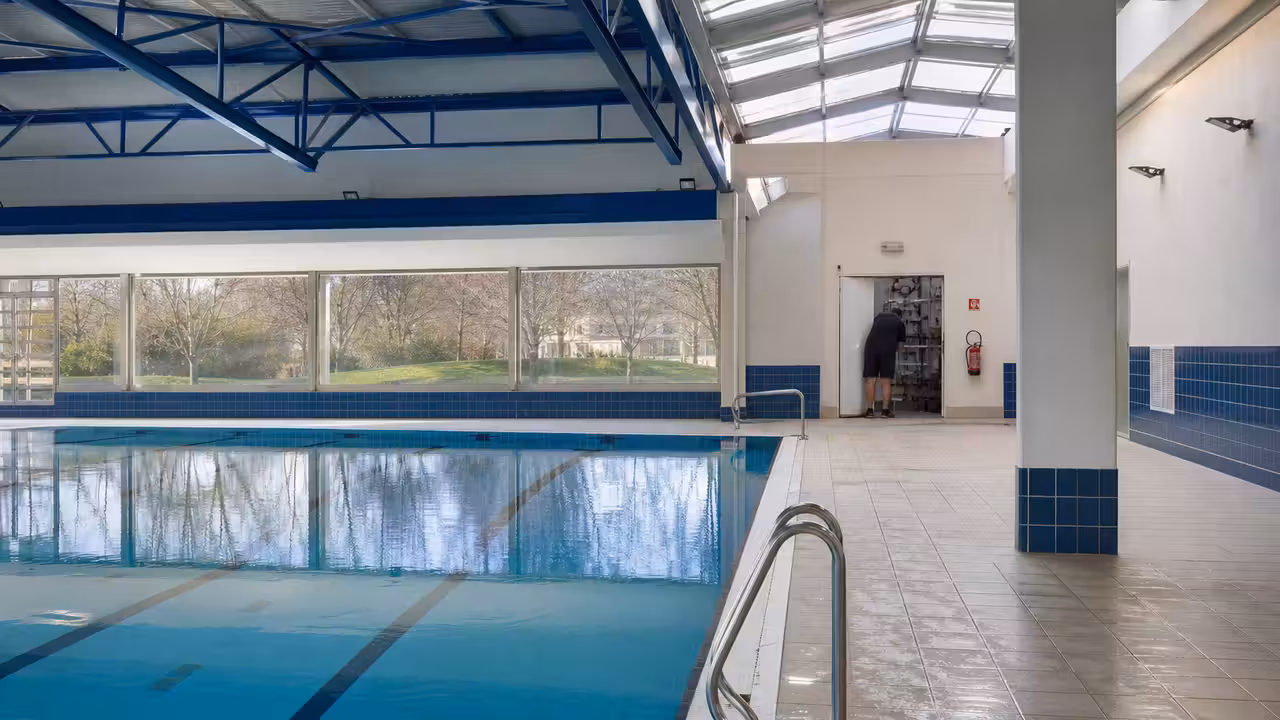 Halle de piscine municipale remise en service, avec bassin calme et technicien vérifiant les équipements