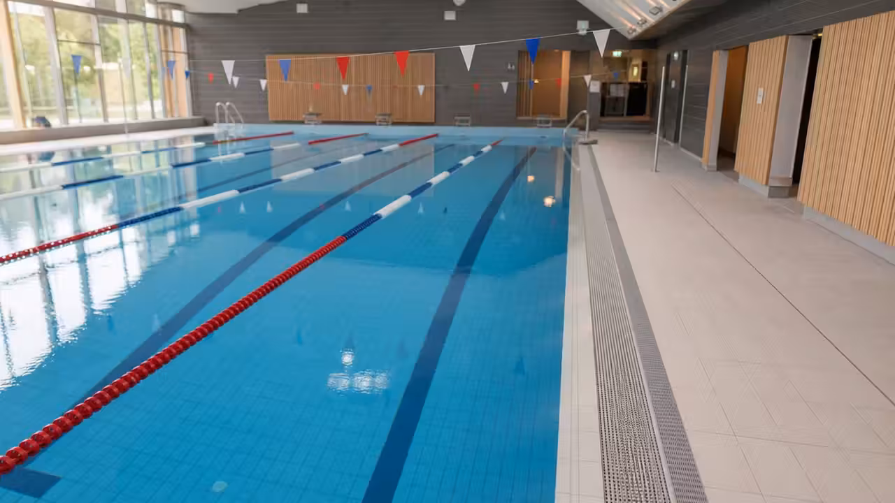 Bassin lumineux d’une piscine municipale rénovée avec lignes d’eau, plages carrelées et grandes baies vitrées